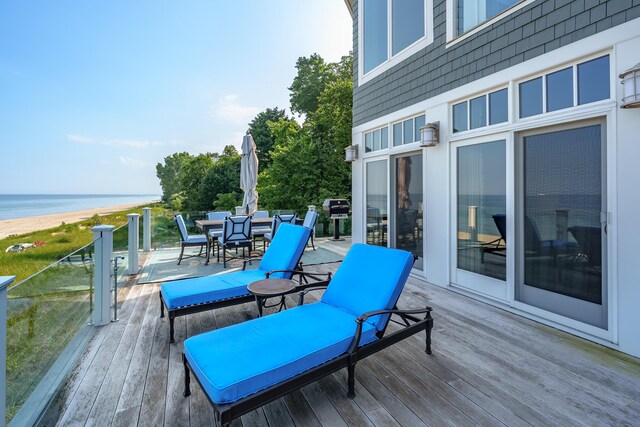 wooden terrace featuring a water view, a view of the beach, and outdoor dining space