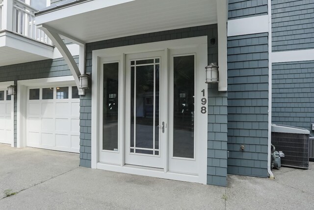 property entrance featuring a balcony, a garage, concrete driveway, and central AC unit