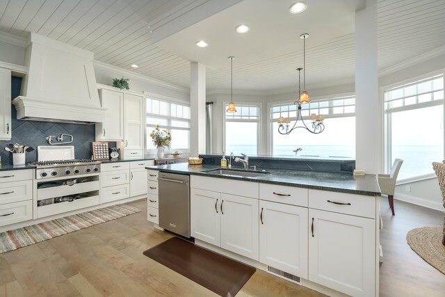 kitchen with light wood finished floors, ornamental molding, tasteful backsplash, a sink, and custom range hood