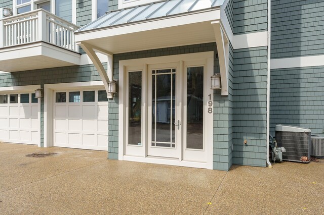 entrance to property featuring a standing seam roof, central air condition unit, metal roof, a balcony, and driveway