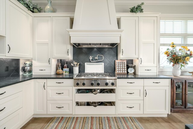 kitchen with light wood finished floors, custom range hood, white cabinets, decorative backsplash, and ornamental molding