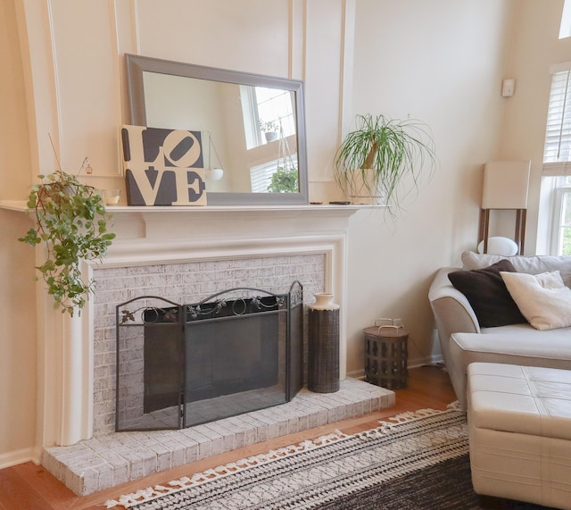 living area featuring a brick fireplace, plenty of natural light, baseboards, and wood finished floors