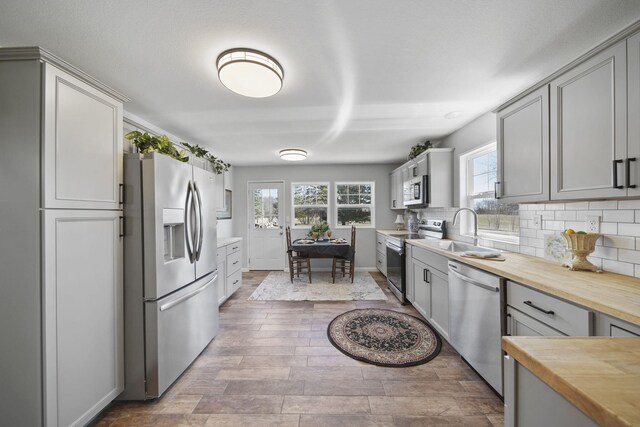 kitchen with gray cabinets, a sink, tasteful backsplash, appliances with stainless steel finishes, and wooden counters