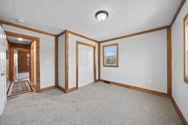 unfurnished bedroom with a closet, carpet flooring, wooden walls, baseboards, and visible vents