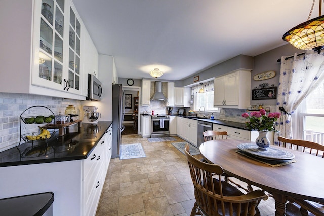 kitchen featuring stainless steel appliances, a sink, dark countertops, wall chimney range hood, and stone finish flooring