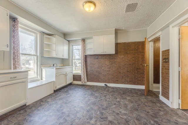 kitchen featuring open shelves, visible vents, baseboards, a textured ceiling, and brick wall