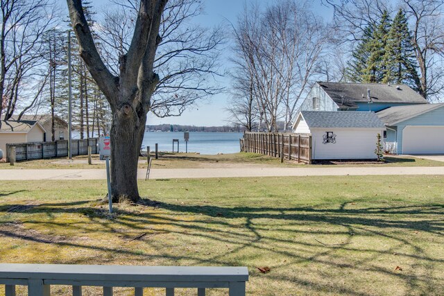 view of yard featuring a water view, fence, a garage, and an outbuilding