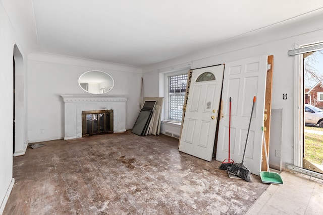 unfurnished living room featuring arched walkways, a glass covered fireplace, and a wealth of natural light