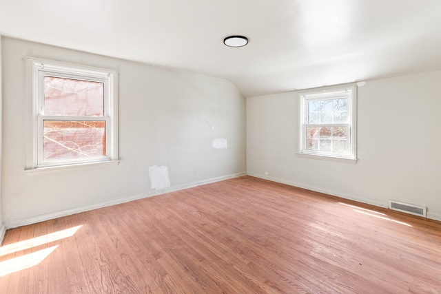 empty room featuring visible vents, baseboards, vaulted ceiling, and wood finished floors