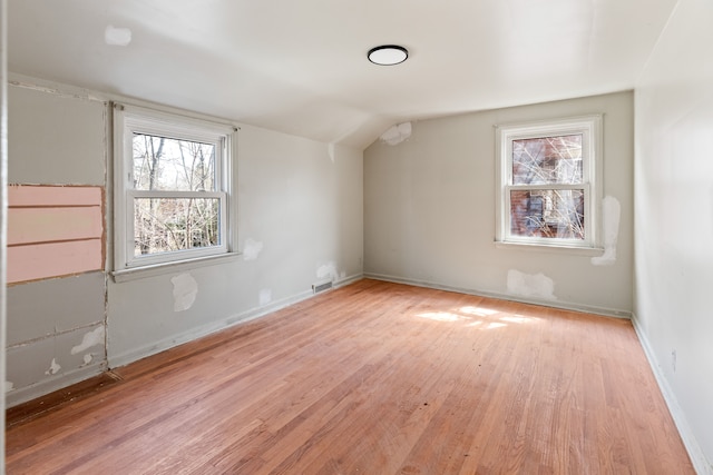 additional living space featuring visible vents, light wood finished floors, baseboards, and vaulted ceiling