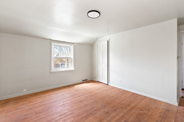 spare room featuring light wood finished floors, visible vents, baseboards, and lofted ceiling