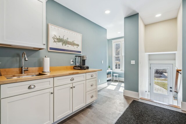 kitchen featuring baseboards, white cabinets, butcher block countertops, and a sink