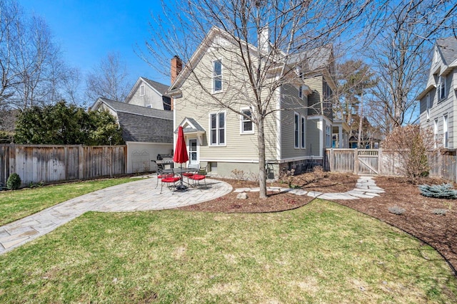 rear view of house with a lawn, a chimney, fence private yard, and a patio area