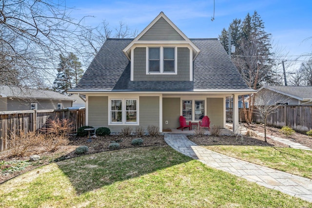 view of front of property featuring a porch, fence, roof with shingles, and a front lawn