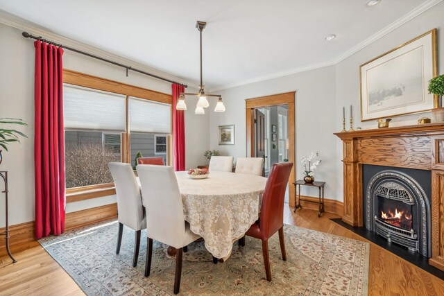 dining room featuring a fireplace with flush hearth, baseboards, crown molding, and wood finished floors