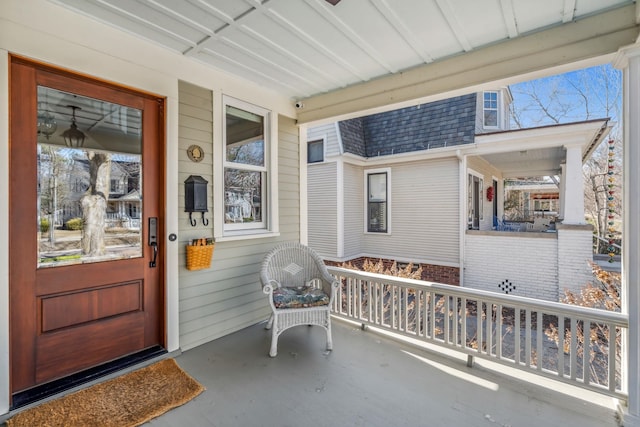 view of exterior entry featuring a shingled roof and covered porch