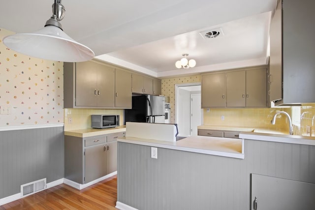 kitchen with freestanding refrigerator, a peninsula, a wainscoted wall, stainless steel microwave, and wallpapered walls