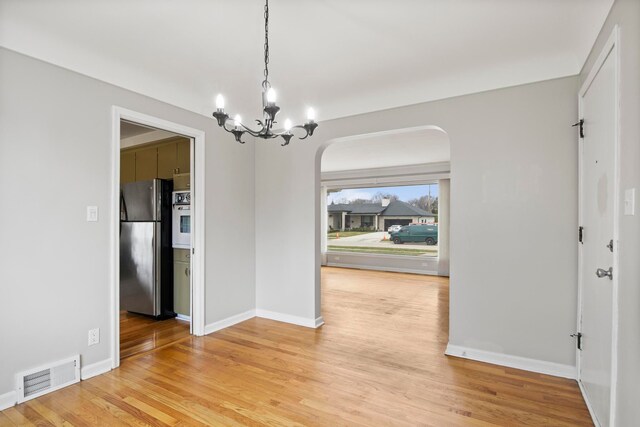 unfurnished dining area with light wood-style floors, arched walkways, visible vents, baseboards, and a notable chandelier
