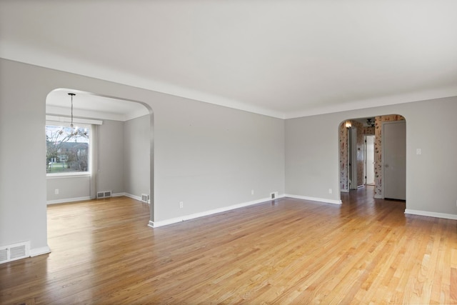 spare room with arched walkways, an inviting chandelier, visible vents, and light wood-type flooring