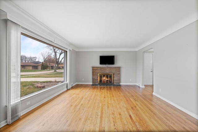 unfurnished living room featuring arched walkways, wood finished floors, baseboards, and a glass covered fireplace