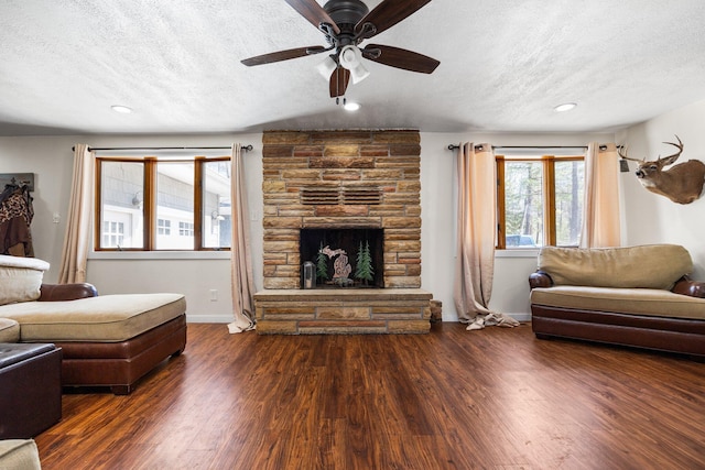 living room featuring a textured ceiling, baseboards, ceiling fan, wood finished floors, and a stone fireplace