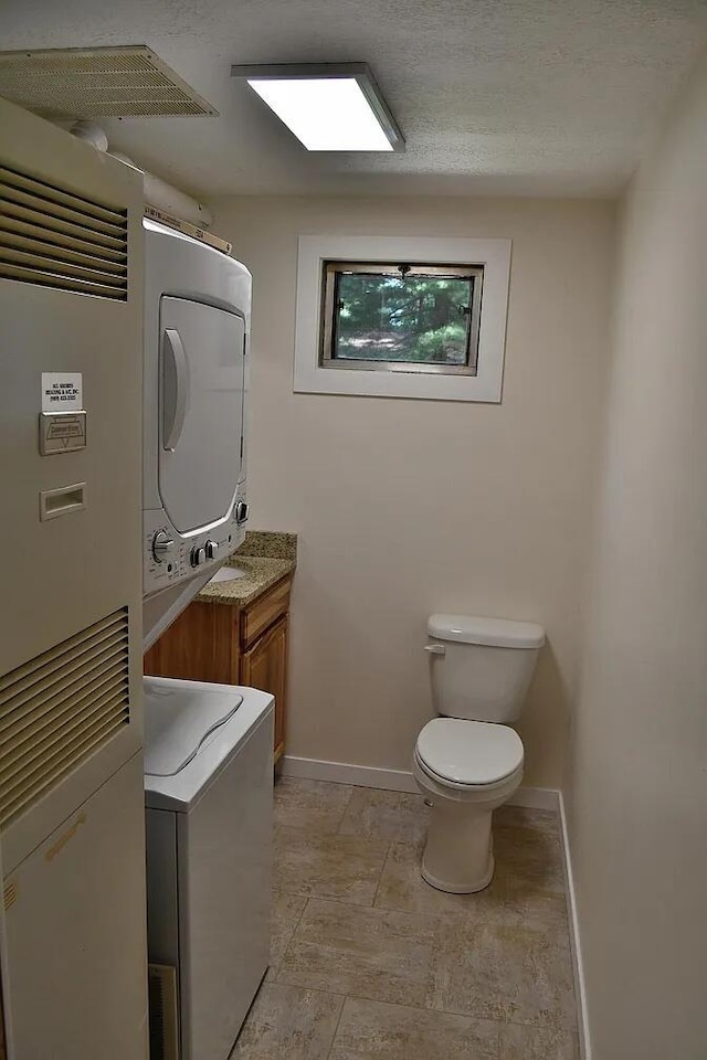 bathroom featuring stacked washer / dryer, toilet, and baseboards