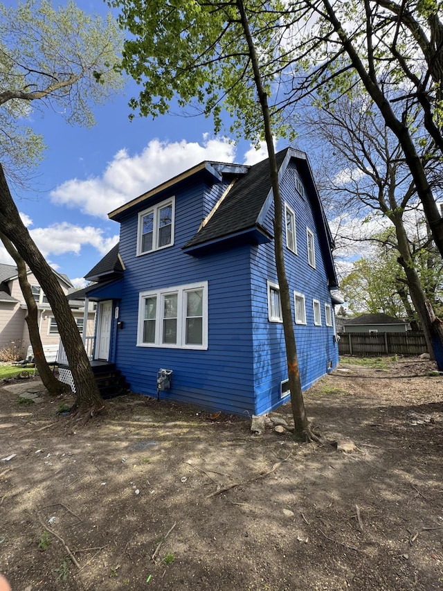 traditional home with driveway, a shingled roof, and fence