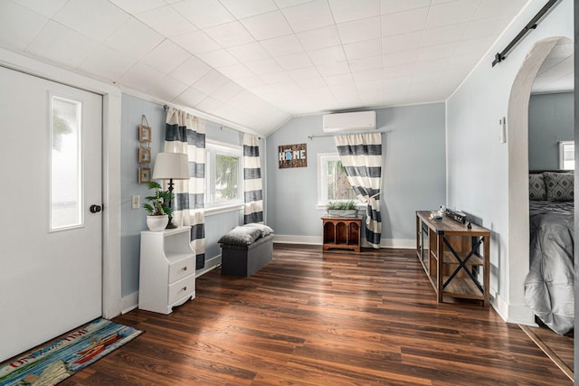 living area with a wall mounted AC, arched walkways, baseboards, and wood finished floors