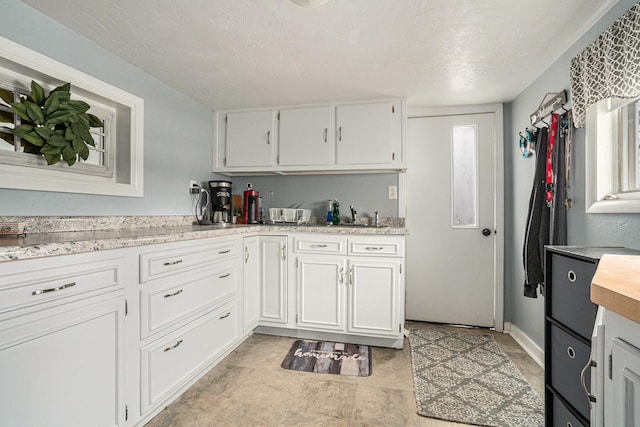 kitchen with a textured ceiling, light countertops, baseboards, and white cabinets