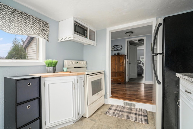 kitchen featuring white range with electric cooktop, white cabinets, freestanding refrigerator, and visible vents