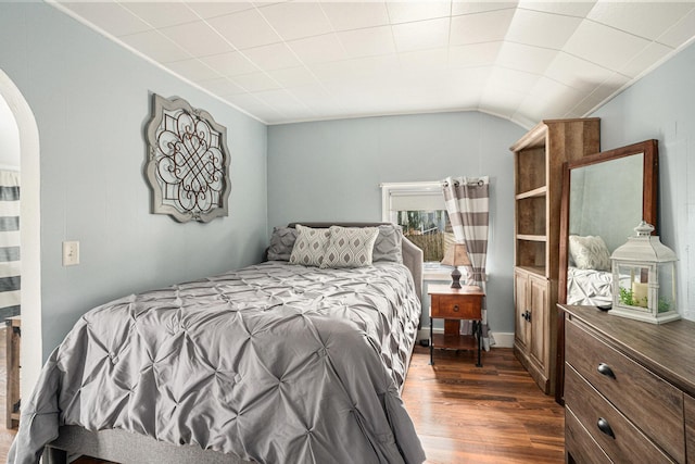 bedroom featuring arched walkways, dark wood-type flooring, and vaulted ceiling