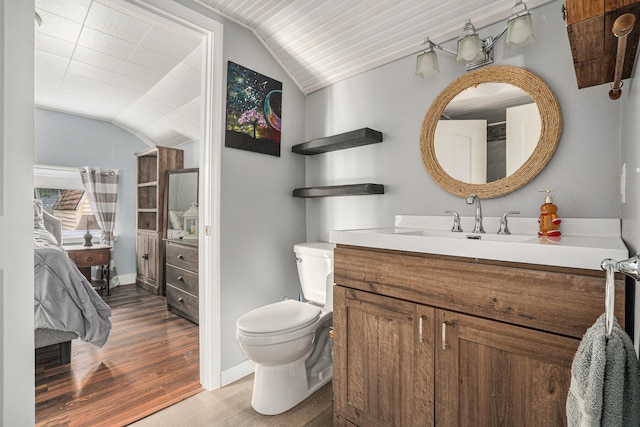 ensuite bathroom featuring toilet, vanity, wood finished floors, lofted ceiling, and ensuite bath