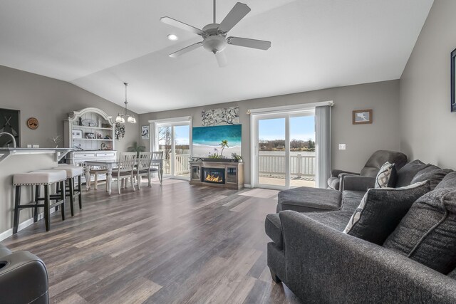 living area featuring ceiling fan with notable chandelier, vaulted ceiling, a wealth of natural light, and dark wood-style floors