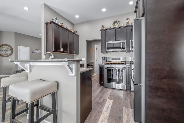 kitchen featuring a peninsula, light wood finished floors, a kitchen bar, recessed lighting, and appliances with stainless steel finishes