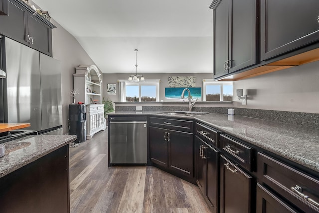 kitchen featuring stainless steel appliances, dark stone countertops, a sink, dark wood-style floors, and vaulted ceiling