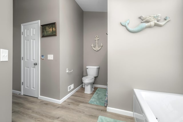 full bathroom with a bath, toilet, baseboards, visible vents, and wood finished floors