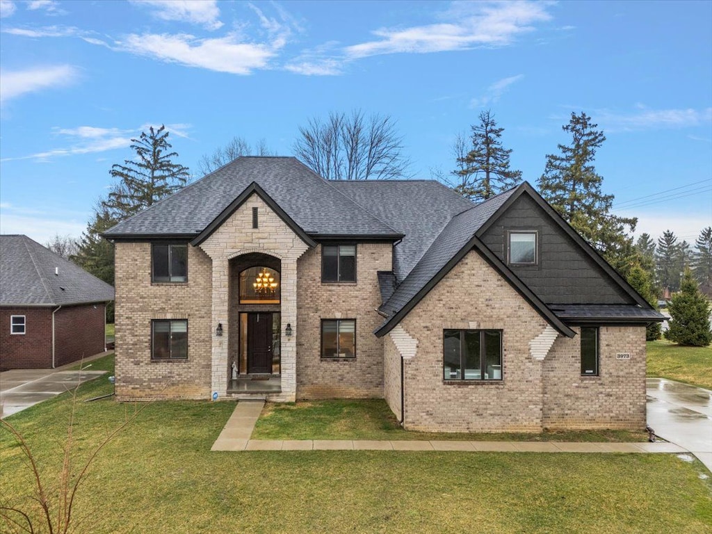 french country home featuring brick siding, a front lawn, and roof with shingles