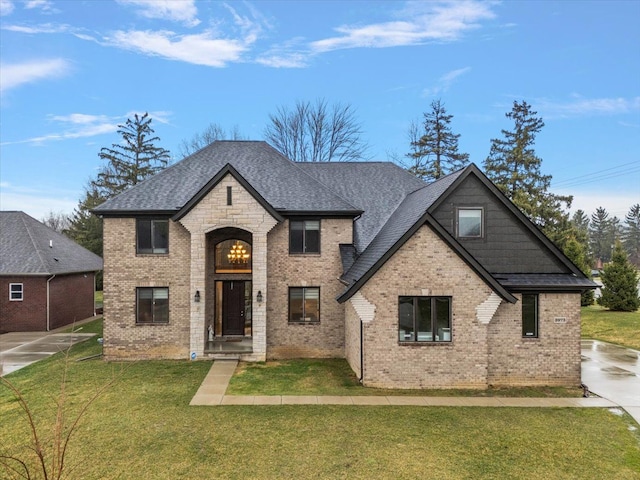 french country home featuring brick siding, a front lawn, and roof with shingles