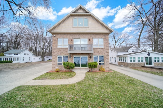 view of property with a balcony, driveway, a front lawn, and brick siding