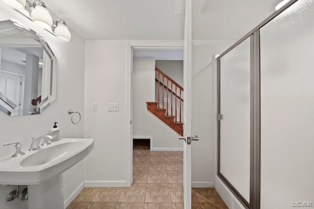 full bathroom featuring a textured ceiling, tile patterned flooring, a stall shower, a sink, and baseboards