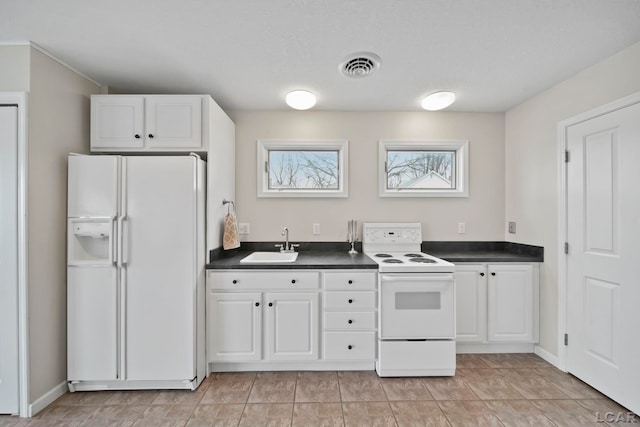 kitchen with visible vents, dark countertops, a sink, white cabinets, and white appliances