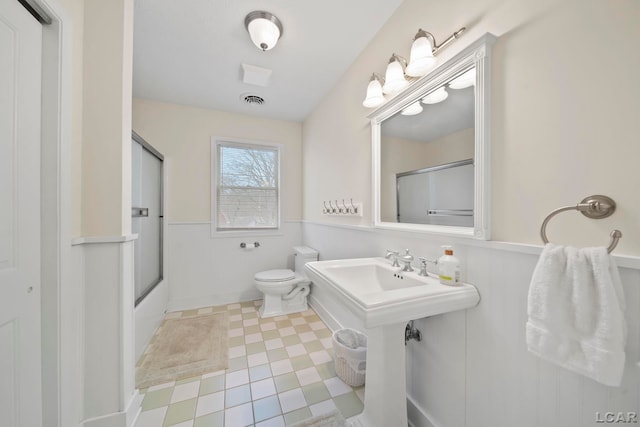 bathroom with enclosed tub / shower combo, wainscoting, and toilet