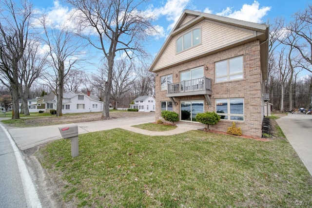 view of front of home with a balcony, a front yard, driveway, and brick siding