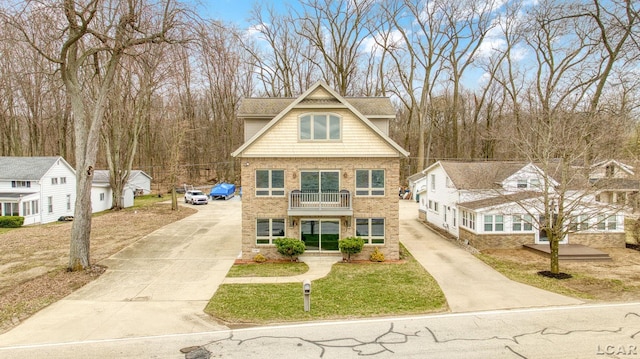 view of front facade with concrete driveway, brick siding, a balcony, and a front yard