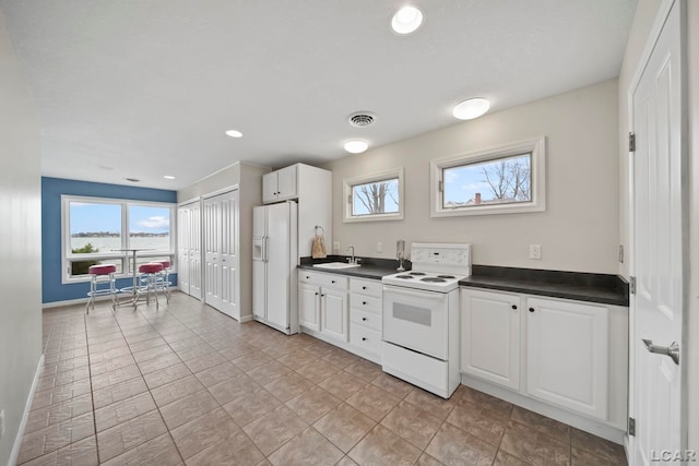 kitchen featuring white appliances, dark countertops, visible vents, and a sink