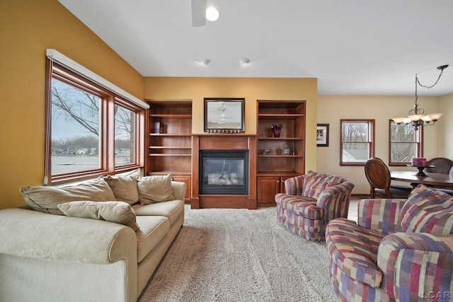 carpeted living room featuring a glass covered fireplace, a healthy amount of sunlight, and a notable chandelier