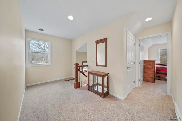 hallway featuring baseboards, visible vents, light carpet, and an upstairs landing