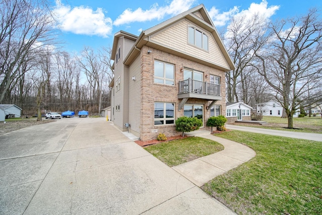 view of front of home featuring brick siding, a balcony, a front yard, and concrete driveway