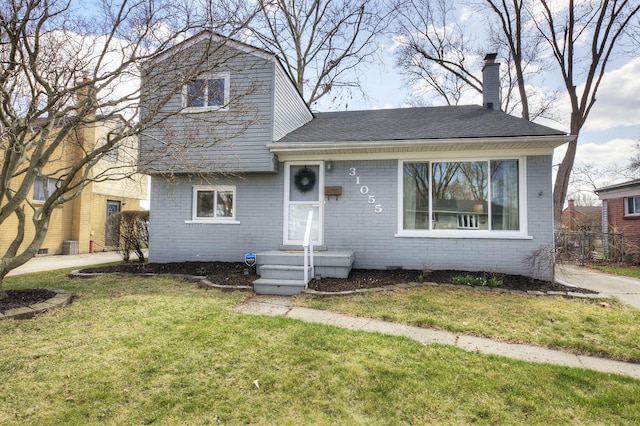 split level home with a chimney, a front yard, brick siding, and roof with shingles