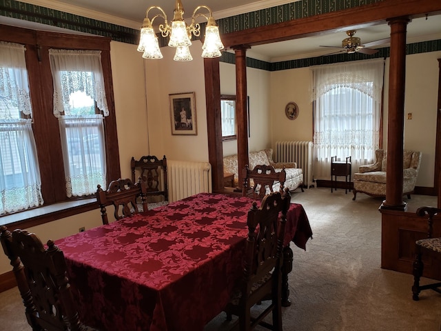 carpeted dining space featuring ornamental molding, decorative columns, radiator, and ceiling fan with notable chandelier